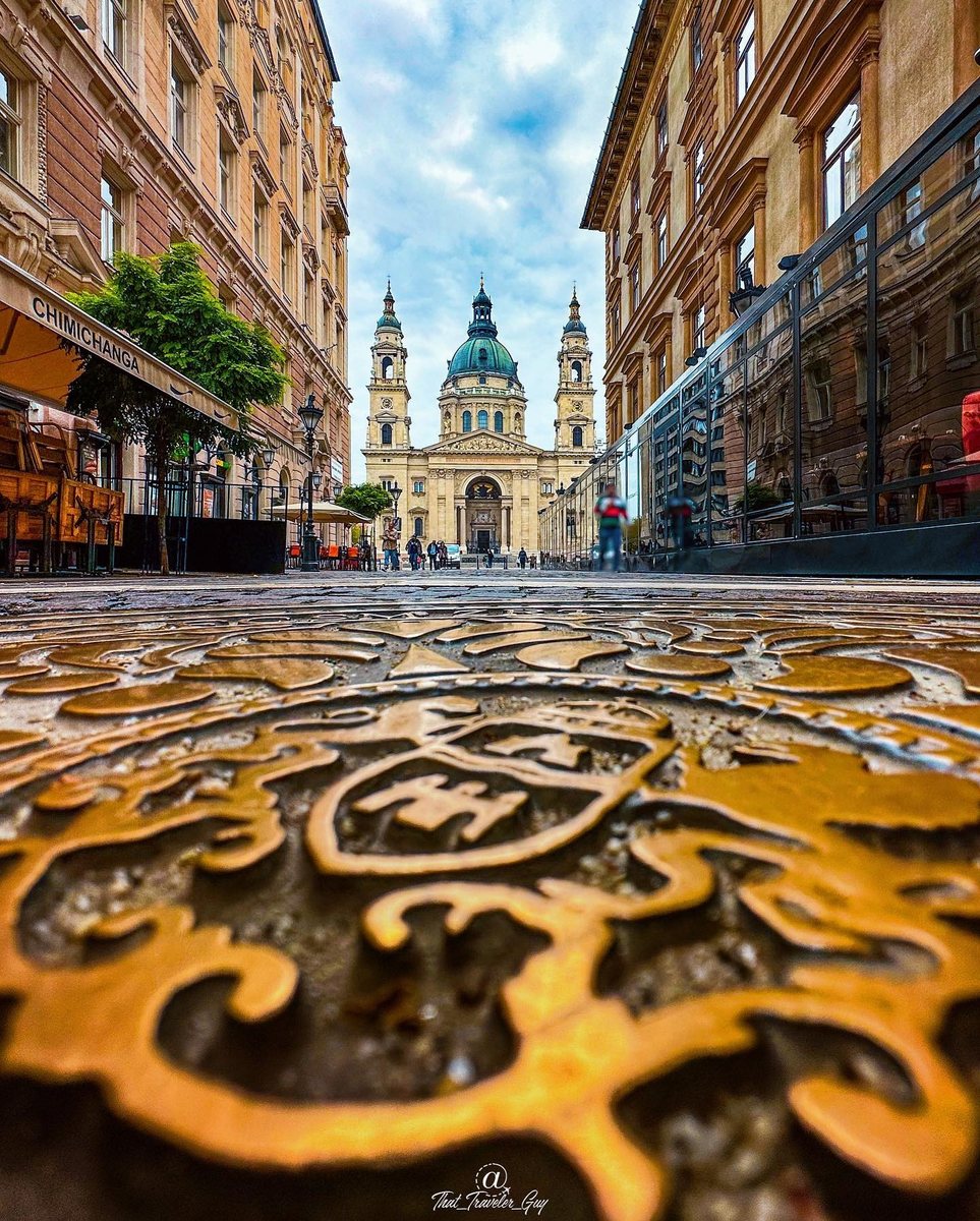 La basilique Saint-Étienne de Budapest vue au ras du sol derrière une plaque d’égout ouvragée